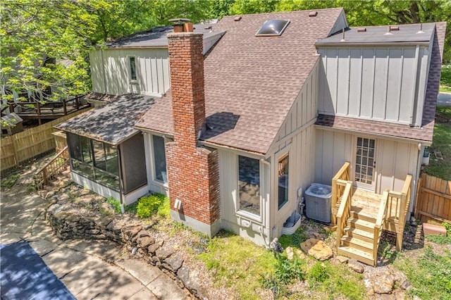 rear view of house with a chimney, board and batten siding, central air condition unit, a sunroom, and a shingled roof
