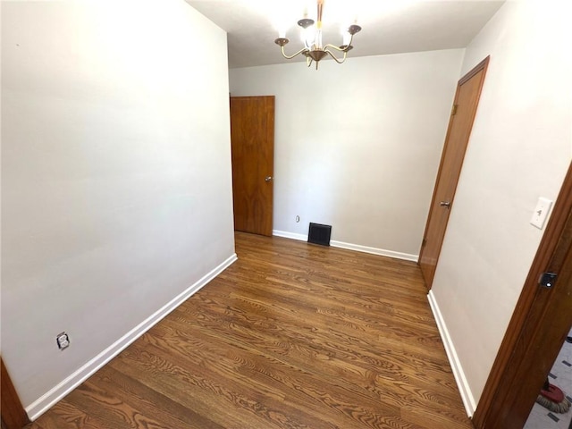 spare room featuring a chandelier, wood finished floors, and baseboards