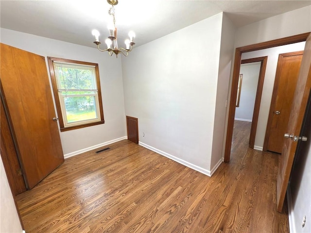 spare room featuring a chandelier, wood finished floors, and baseboards