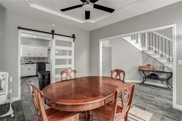 6700 N Charlston Dr, Kansas City, MO 64119 - dining space featuring a barn door, a ceiling fan, a raised ceiling, wood finished floors, and baseboards