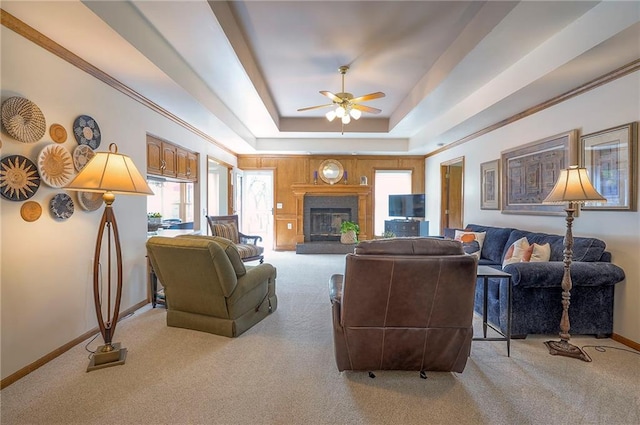 living room with light colored carpet, a raised ceiling, a ceiling fan, baseboards, and a glass covered fireplace