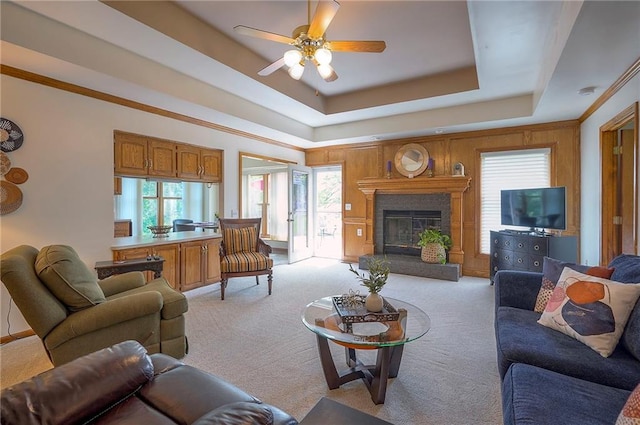 living area with a raised ceiling, light colored carpet, a glass covered fireplace, and ceiling fan