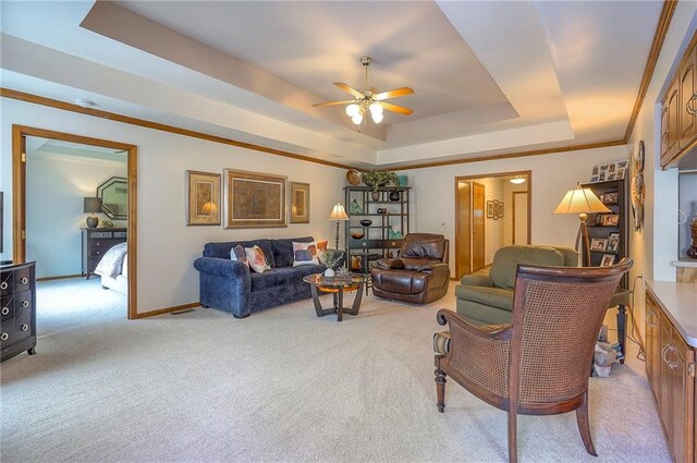 living room with a tray ceiling, a ceiling fan, light carpet, and baseboards