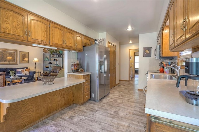 kitchen with brown cabinetry, stainless steel refrigerator with ice dispenser, light wood finished floors, and light countertops