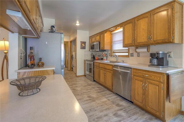 kitchen with stainless steel appliances, a sink, light wood-style floors, and light countertops