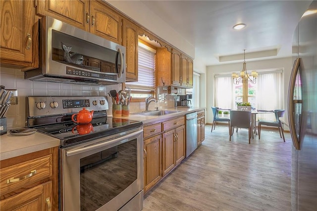kitchen featuring appliances with stainless steel finishes, a sink, brown cabinetry, and light wood finished floors