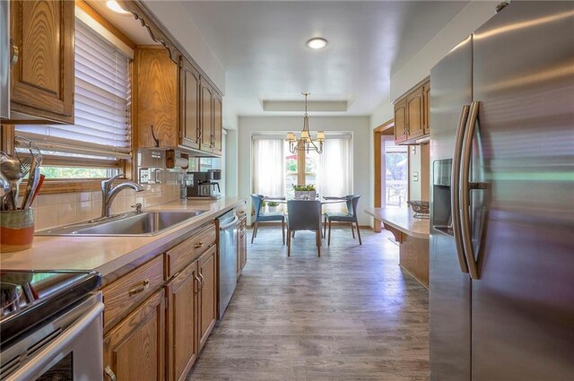 kitchen featuring appliances with stainless steel finishes, a sink, wood finished floors, and brown cabinetry