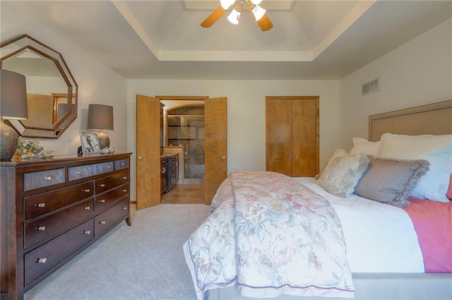 bedroom featuring a tray ceiling, light carpet, a ceiling fan, and connected bathroom