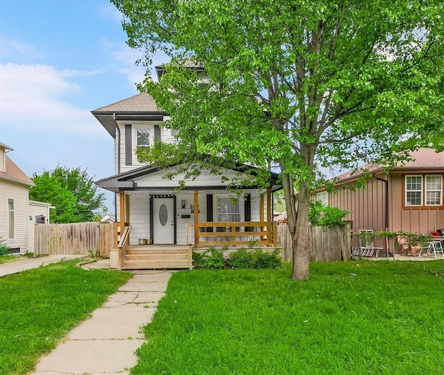 traditional style home with covered porch, fence, and a front yard