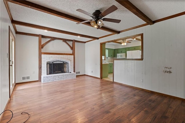 515 London Way, Belton, MO 64012 - unfurnished living room with a ceiling fan, beamed ceiling, wood finished floors, a textured ceiling, and a fireplace