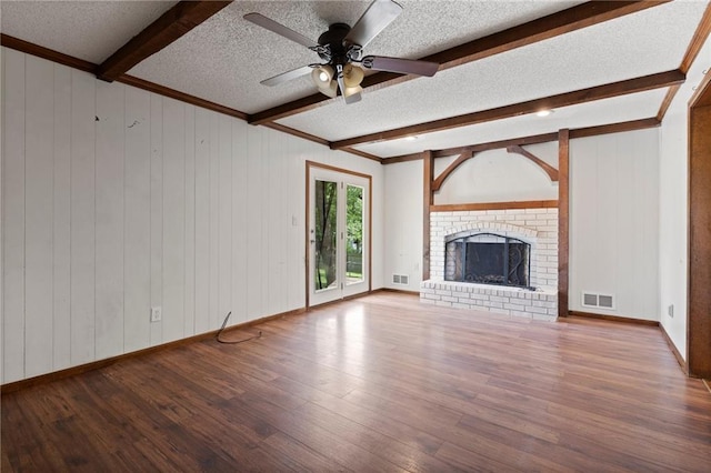 515 London Way, Belton, MO 64012 - unfurnished living room featuring beamed ceiling, wood finished floors, a textured ceiling, a ceiling fan, and a brick fireplace