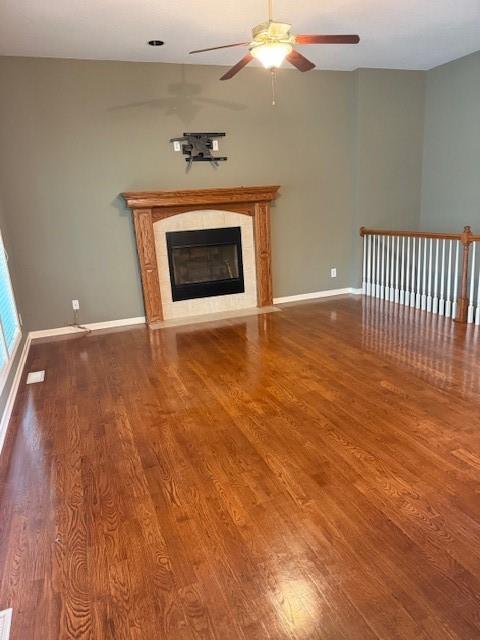 unfurnished living room with a ceiling fan, baseboards, a tiled fireplace, and wood finished floors