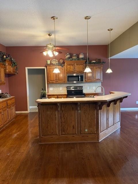kitchen featuring baseboards, appliances with stainless steel finishes, a ceiling fan, and dark wood-type flooring