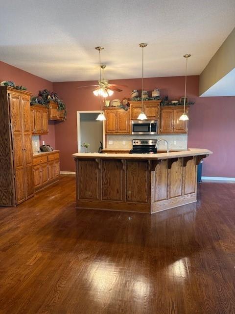 kitchen with brown cabinetry, dark wood-style flooring, light countertops, appliances with stainless steel finishes, and tasteful backsplash