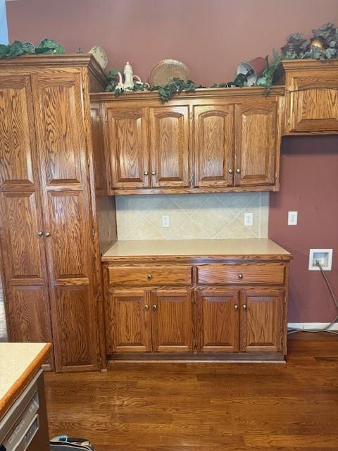 kitchen with dark wood-style flooring, brown cabinets, and backsplash