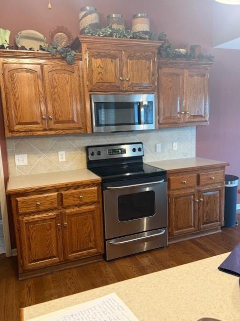 kitchen with dark wood-style flooring, decorative backsplash, light countertops, and appliances with stainless steel finishes