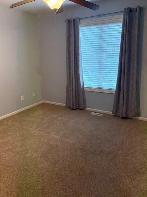 carpeted empty room with baseboards, visible vents, and ceiling fan
