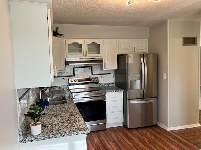 kitchen with under cabinet range hood, dark wood-style flooring, visible vents, backsplash, and stainless steel appliances