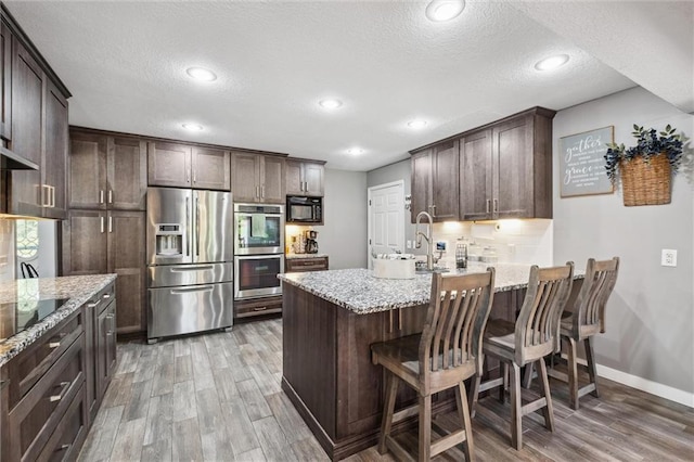 17201 NE 136th St, Kearney, MO 64060 - kitchen featuring black appliances, light wood-style flooring, dark brown cabinets, a peninsula, and light stone counters