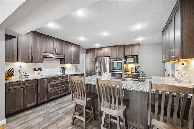 17201 NE 136th St, Kearney, MO 64060 - kitchen featuring black appliances, under cabinet range hood, dark brown cabinetry, light wood finished floors, and light stone countertops