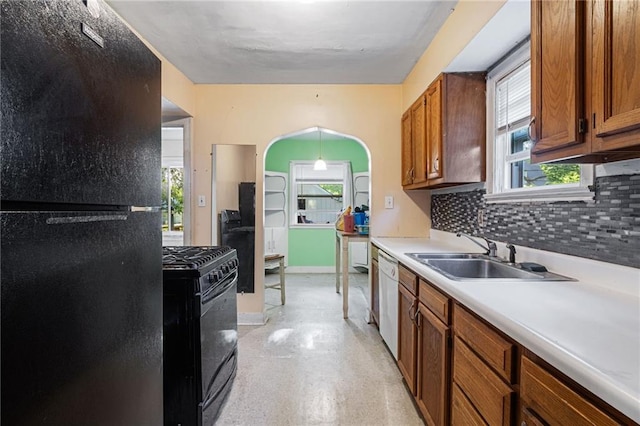 kitchen featuring black appliances, a sink, arched walkways, decorative backsplash, and brown cabinetry