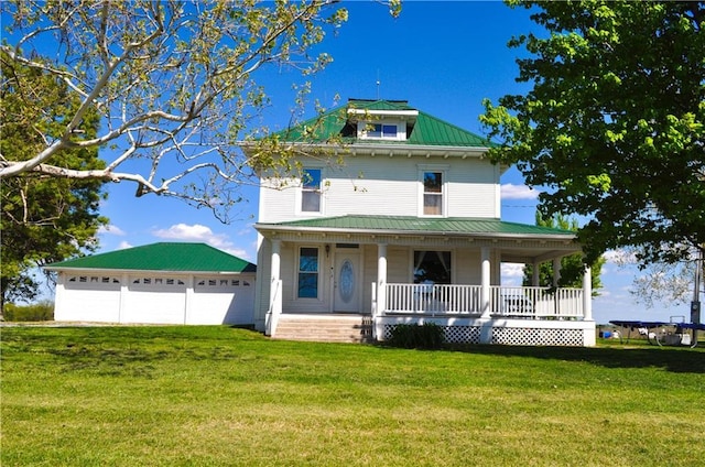 view of front of house featuring a front yard, covered porch, metal roof, and a detached garage