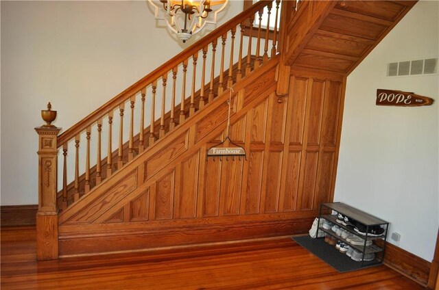 staircase with vaulted ceiling, an inviting chandelier, visible vents, and wood finished floors