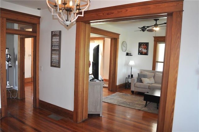 hallway with baseboards, dark wood finished floors, and a chandelier