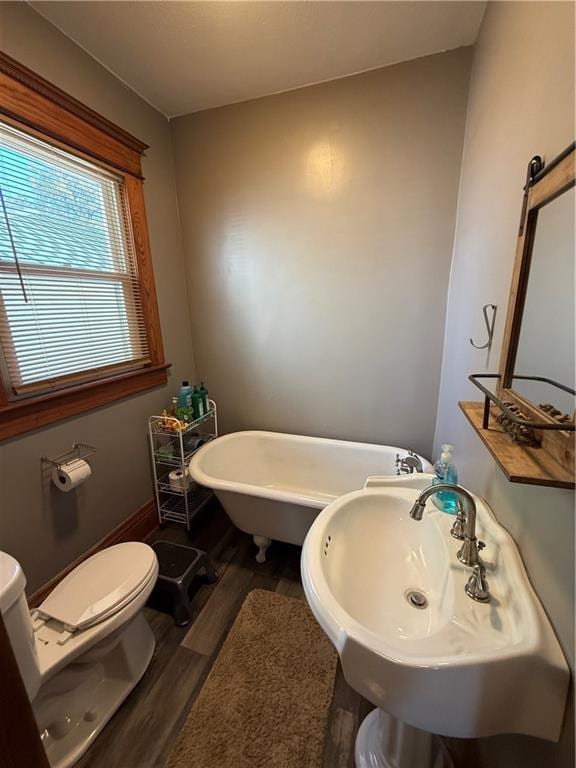 bathroom featuring toilet, wood finished floors, a sink, baseboards, and a freestanding tub