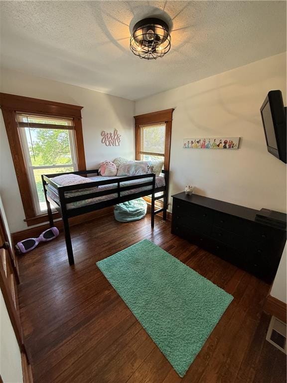 bedroom with a textured ceiling, dark wood-type flooring, baseboards, and visible vents