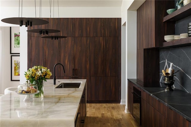 kitchen with modern cabinets, a sink, open shelves, black appliances, and light stone counters