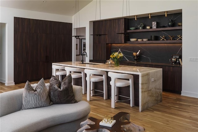 bar area with a sink, light wood-type flooring, baseboards, vaulted ceiling, and backsplash