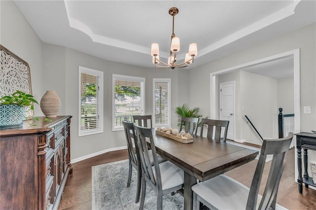dining area featuring a raised ceiling, a chandelier, dark wood-type flooring, and baseboards