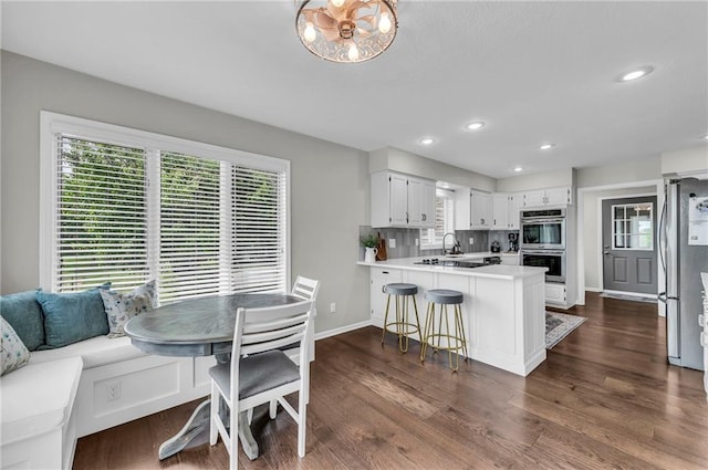 kitchen with appliances with stainless steel finishes, a peninsula, light countertops, dark wood-style floors, and recessed lighting