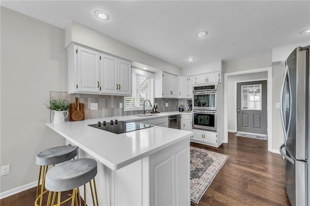 kitchen featuring appliances with stainless steel finishes, a peninsula, backsplash, light countertops, and white cabinetry