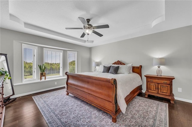 bedroom featuring hardwood / wood-style flooring, baseboards, a tray ceiling, and ceiling fan