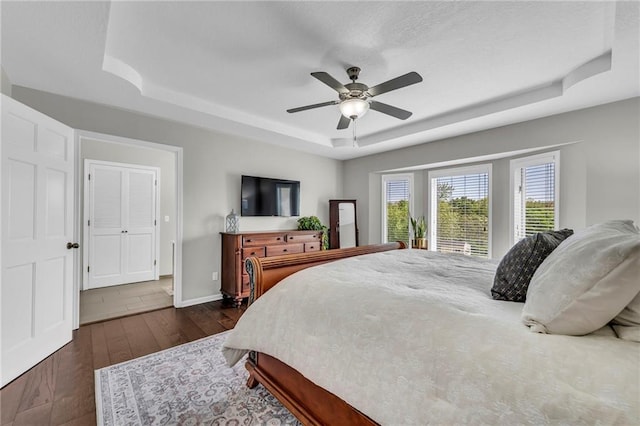 bedroom featuring a raised ceiling, dark wood-style floors, ceiling fan, and baseboards