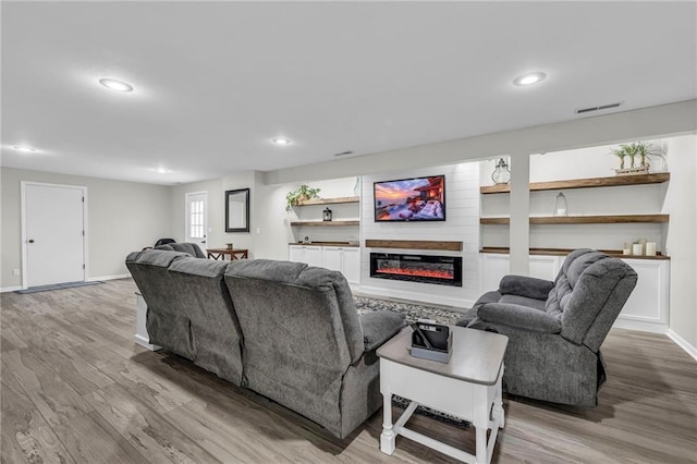 living area with wood finished floors, a glass covered fireplace, recessed lighting, and baseboards