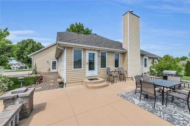 back of property with a patio, a chimney, outdoor dining area, and roof with shingles