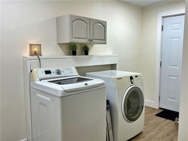 clothes washing area featuring washer and clothes dryer, cabinet space, baseboards, and light wood-style floors