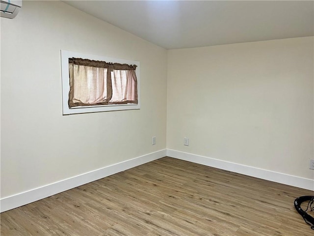 spare room featuring lofted ceiling, a wall mounted AC, baseboards, and wood finished floors