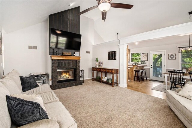 carpeted living area featuring baseboards, visible vents, ceiling fan, a brick fireplace, and high vaulted ceiling