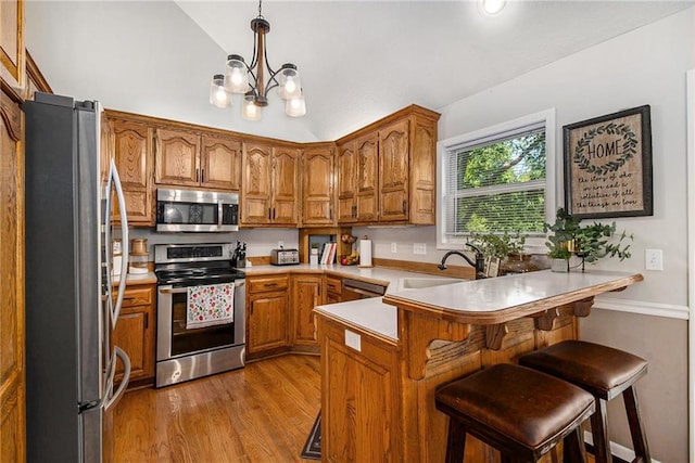 kitchen with a peninsula, wood finished floors, stainless steel appliances, and brown cabinetry