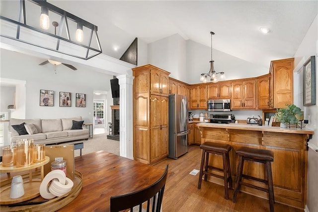 kitchen with a peninsula, ceiling fan with notable chandelier, high vaulted ceiling, stainless steel appliances, and brown cabinetry