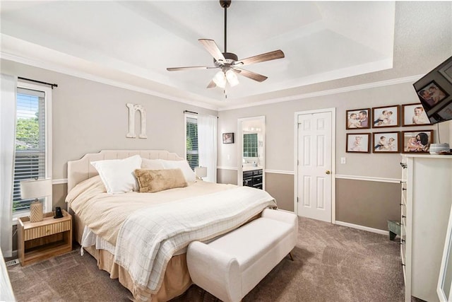 bedroom featuring a ceiling fan, a tray ceiling, baseboards, ensuite bathroom, and carpet flooring