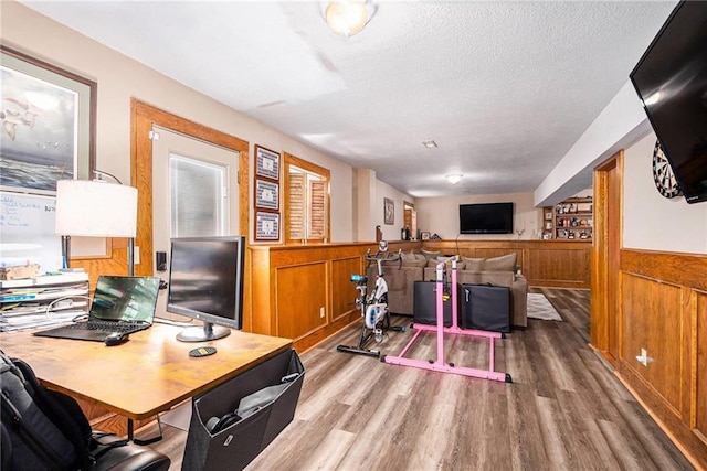 office area featuring a textured ceiling, a wainscoted wall, and wood finished floors