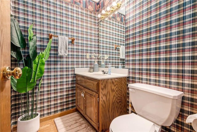 half bath with toilet, wallpapered walls, and wood finished floors