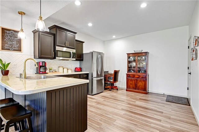 8904 NE 94th Pl, Kansas City, MO 64157 - kitchen featuring stainless steel appliances, a sink, light countertops, a kitchen bar, and light wood-style flooring