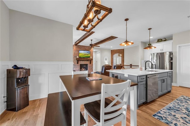 kitchen with stainless steel appliances, gray cabinetry, a brick fireplace, light wood-style flooring, and a center island with sink