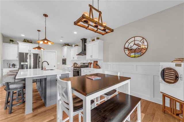 kitchen with appliances with stainless steel finishes, wall chimney exhaust hood, washer / dryer, a sink, and light wood-style floors
